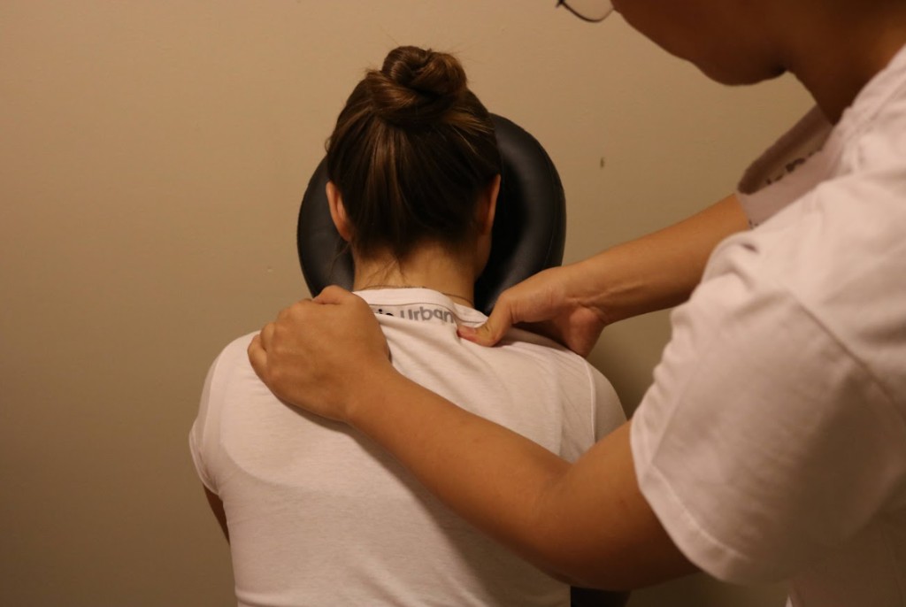 Sessão de Shiatsu no Yoga du Ville: terapeuta aplicando pressão nos ombros de uma cliente em cadeira de massagem, Tijuca